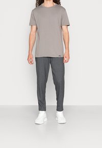 Grijze crew-neck t-shirt gecombineerd met donker gestreepte broek en witte sneakers. Gladde stof, relaxte pasvorm en contrasterende verticale strepen.