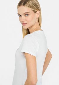 Hvid kortærmet t-shirt med rund hals, glat stoftekstur, tætsiddende pasform og med et subtilt grafisk design på fronten.