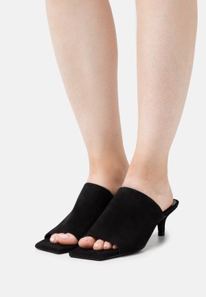 Zwarte suède open-tegen mules met een vierkante vorm, voorzien van een brede bovenkant en een taps toelopende hak. Glad textuur en minimalistisch ontwerp.