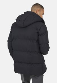 Zwarte pufferjack met een gestructureerde afwerking, capuchon en een knielange snit met horizontale baffle-stiksel. Ritszakken aan de zijkanten.