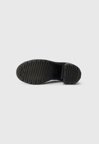 Sole in gomma nera con un motivo testurizzato caratterizzato da scanalature orizzontali e verticali per trazione e grip. Profilo piatto.