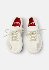 Hvite sneakers med et pustende mesh-overdel, teksturerte detaljer og lyse grå lissesnorer. Røde såler har "CAMPER"-logoen. Rund tådesign.