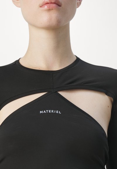 Black top made of smooth fabric featuring a cut-out design. Displays the brand "MATERIEL" in white text at the chest area.
