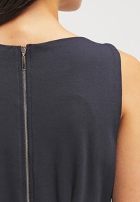 Abito senza maniche di colore blu navy con una texture liscia, dotato di una cerniera metallica centrale sul retro. Design minimalista, scollatura rotonda semplice.