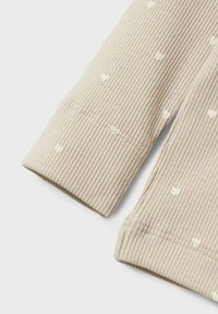Ribbed beige kangas yenye mifumo midogo ya moyo mweupe, ikiwa na uso wenye muundo na mikono iliyonyooka.