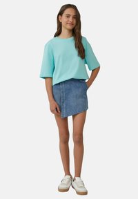 Turkoois kortmouwen shirt gecombineerd met een denim wikkelrok, met rafelige randen. Draagt witte sneakers met een rubberen zool.