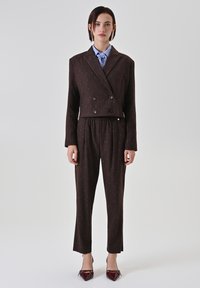 Doppelreihiger brauner Blazer mit dezenten Nadelstreifen, kombiniert mit passenden Hosen, akzentuiert durch ein hellblaues Hemd mit Kragen und burgunderrote High Heels.