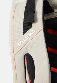 Beige rugtasband van textuurstof met zwarte accenten, voorzien van een witte "SALEWA"-logo en een uitsparing voor aanpassing.