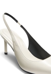Chaussure à talon haut à bride arrière en cuir blanc avec un talon fin et une doublure intérieure noire, présentée sur un fond blanc.