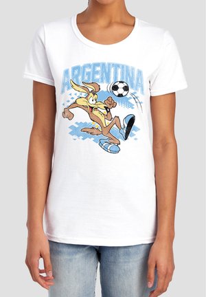 Person trägt ein weißes T-Shirt mit einem Cartoon-Kojoten, der einen Fußball tritt, und dem Wort Argentinien in blauer Schrift darüber.