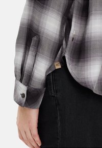 Schwarz-weiß kariertes Hemd mit langen Ärmeln, knöpfbaren Manschetten und strukturiertem Stoff. Verfügt über ein kleines Markenlabel in der Nähe der Naht.