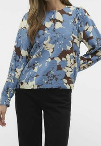 Blaue Bluse mit floralem Muster und cremefarbenen sowie braunen Akzenten, die lange Ärmel, einen runden Ausschnitt und einen strukturierten Stoff mit subtiler Schimmeroptik aufweist.