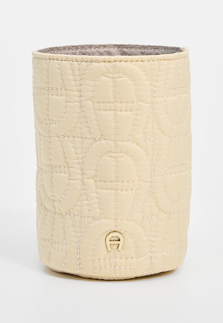 Contenedor de tela beige con acolchado y forma cilíndrica, con patrones de costura y un sutil detalle del logo en la base.