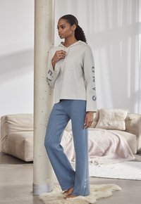 Lichtgrijs cropped hoodie met "SAND" op de mouwen, gecombineerd met losse blauwe sweatpants met "ELB" logo. Zachte textuur, casual ontwerp.