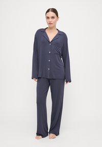 Navy pajama set made of soft fabric, featuring long-sleeved button-up top with pocket and relaxed fit pants with straight legs.