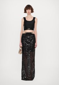 Black crop top with a circular gold accent at the waist, paired with a floor-length black sequined skirt featuring wavy texture.