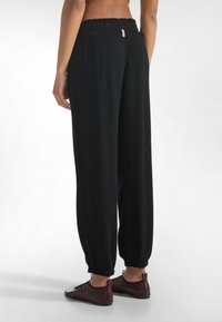 Mustat collegehousut, joissa on joustava vyötärönauha ja kerätyt lahkeet, valmistettu pehmeästä kankaasta. Minimalistinen design ilman näkyviä kuvioita tai lisävarusteita.