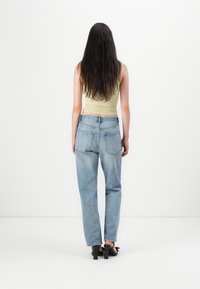 Débardeur vert clair au design ajusté, associé à un jean droit bleu clair. Taille élastique et poches arrière standards visibles.