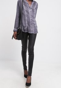 Blusa a maniche lunghe in lavanda con scollo a V, tasche applicate, abbinata a leggings in pelle nera e scarpe con tacco nere.