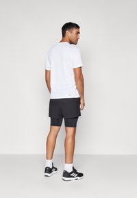 Weißes Kurzarmhemd kombiniert mit schwarzen Sportshorts und Schuhen, das ein sportliches Design und eine entspannte Passform zeigt.