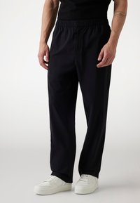 Black elastic waist pants with a relaxed fit, made from lightweight fabric. Features front pockets and is paired with white sneakers.