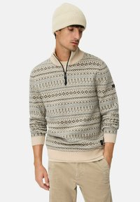 Beige en bruin gemêleerd gebreid sweater met een hoge kraag en ritssluiting. Draag met een bijpassende beige beanie en lichtgekleurde corduroy broek.