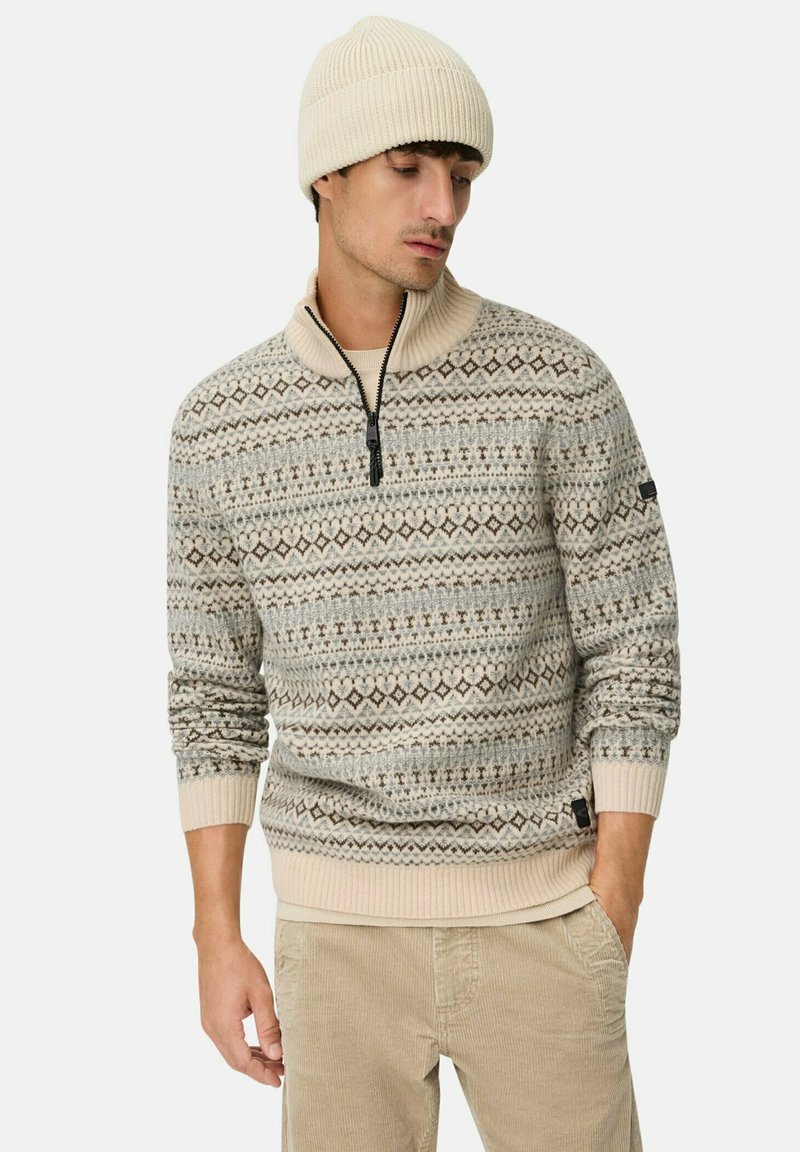 Beige en bruin gemêleerd gebreid sweater met een hoge kraag en ritssluiting. Draag met een bijpassende beige beanie en lichtgekleurde corduroy broek.