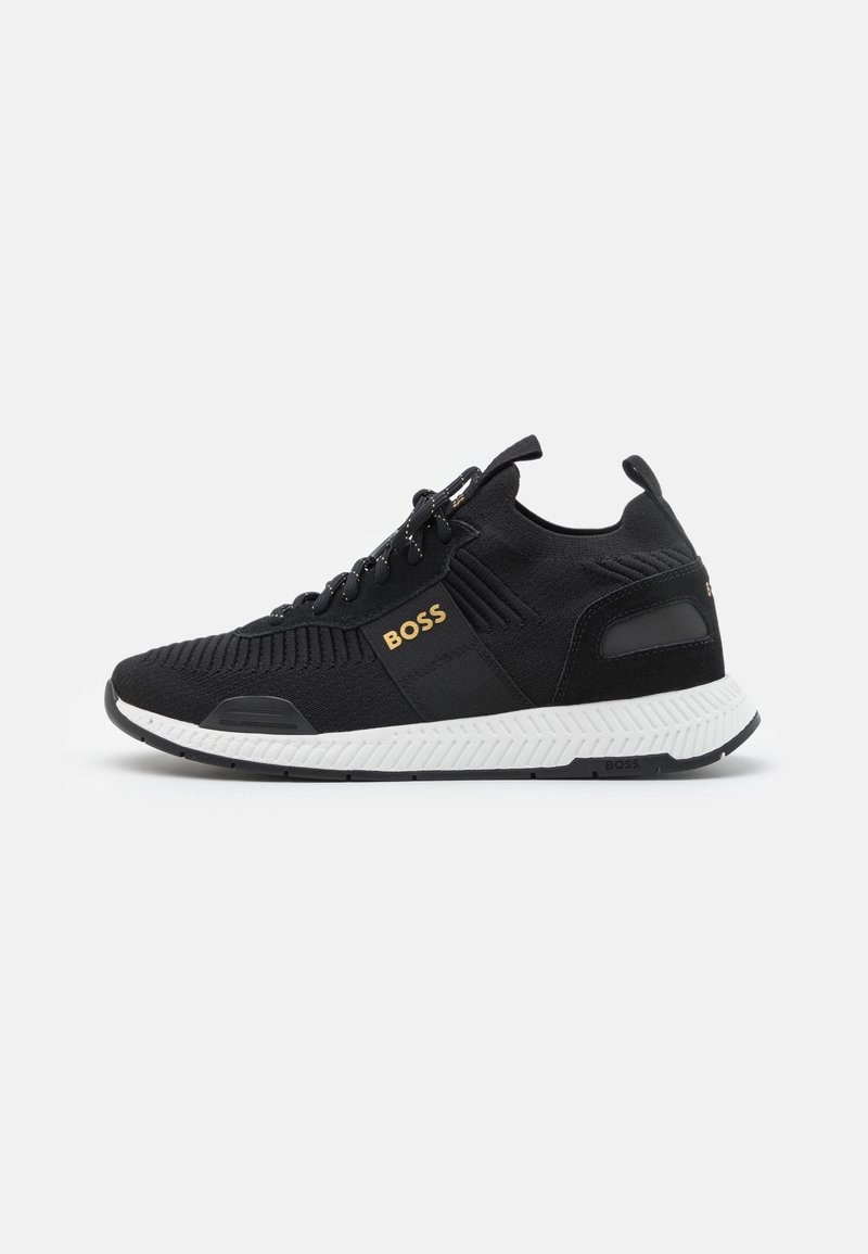 Black athletic shoes with knit upper, textured design, white sole, and gold logo detail. Features lace-up closure and padded collar.
