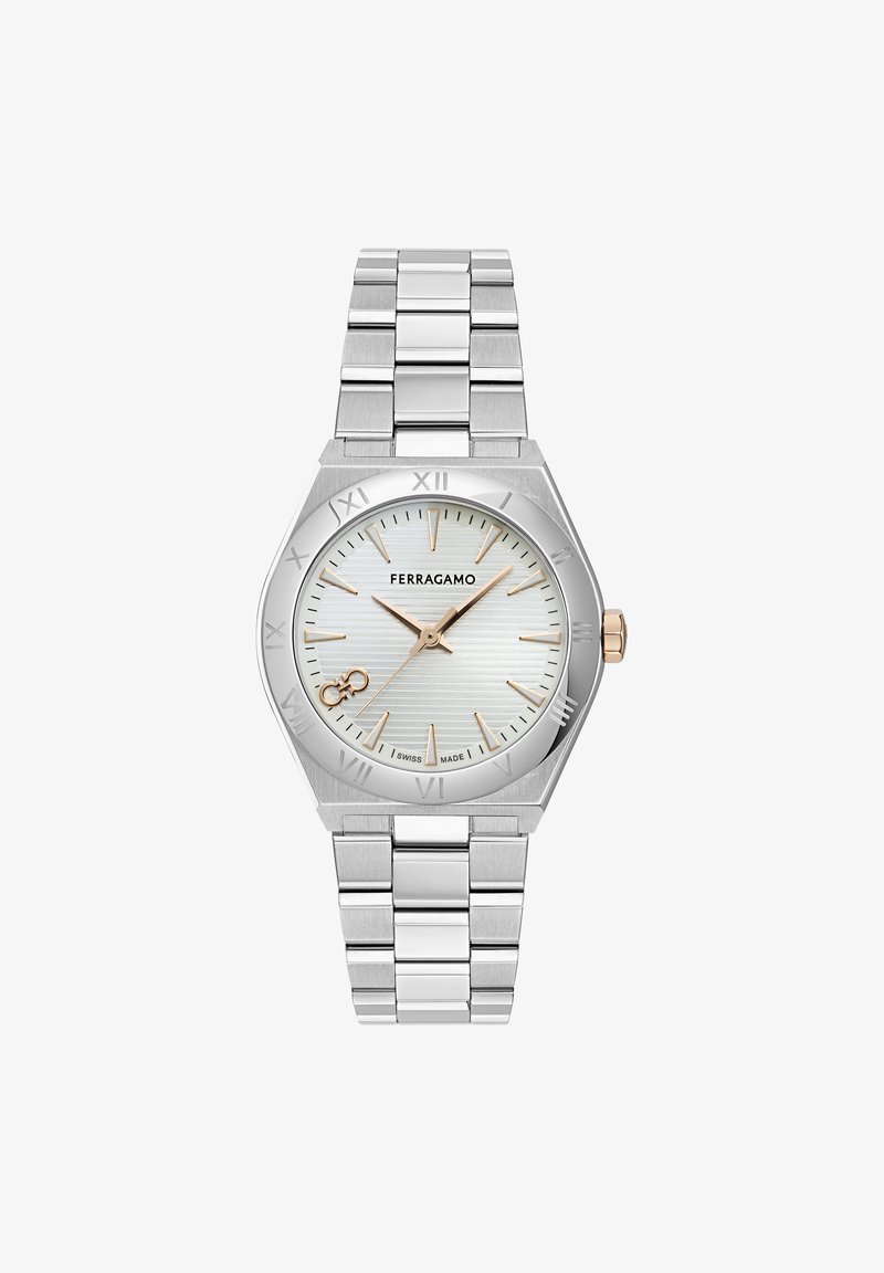 Hõbedane roostevabast terasest kell oktogonaalse korpuse ja valge tekstuuriga kellatäidisega, romaani numbritega ning kuldse tooni aktsentidega kätes ja kroonil.