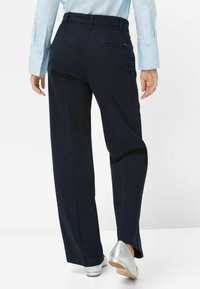 Pantalons larges bleu marine avec une texture lisse, dotés de deux poches arrière et d'une taille avec passants de ceinture. Associés à des talons argentés.