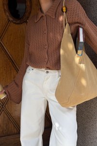 Brown, knitted button-up cardigan with a collar; white wide-leg jeans; slouchy tan bag holding a book; textured fabric details visible.