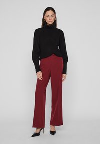 Melnas ribotas turtlenecka tipa džemperis kopā ar bordo platām biksēm un melnām šaurām virsotnes kurpēm. Gluda auduma ar brīvu piegriezumu.