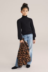 Fekete bordás garbó, világoskék, csípőn gasszal rendelkező farmernadrág és fekete bokacsizma. Egy világosbarna-fekete leopárdmintás kabátot tart. Egyszerű háttér.