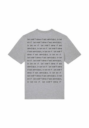 Grijze katoenen t-shirt met herhaaldelijk zwarte tekst: "Ze wist niet dat het onmogelijk was, dus deed ze het." Korte mouwen, klassieke snit.