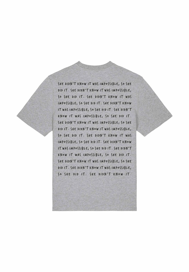 T-shirt en coton gris avec un texte noir répété : "Elle ne savait pas que c'était impossible, alors elle l'a fait." Manches courtes, coupe classique.