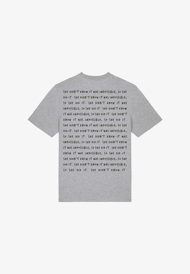 T-shirt en coton gris avec un texte noir répété : "Elle ne savait pas que c'était impossible, alors elle l'a fait." Manches courtes, coupe classique.