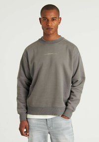 Grå sweatshirt med rund hals, afslappet pasform og subtil branding over brystet. Blødt, tekstureret stof med ribbede manchetter og nederkant.