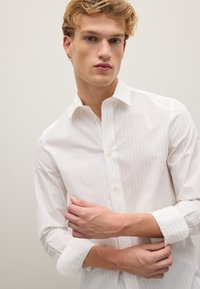 Camicia bianca a righe sottili realizzata in tessuto leggero, con colletto button-down, maniche lunghe e design slim fit.