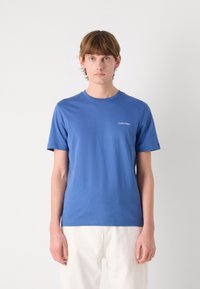Blue cotton t-shirt with short sleeves, crew neckline, and subtle white Calvin Klein logo on the left chest area. Smooth texture.