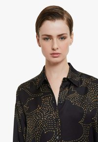 Camicia nera con colletto alla coreana con bottoni, caratterizzata da un motivo astratto dorato. Tessuto morbido con trama liscia e vestibilità rilassata.