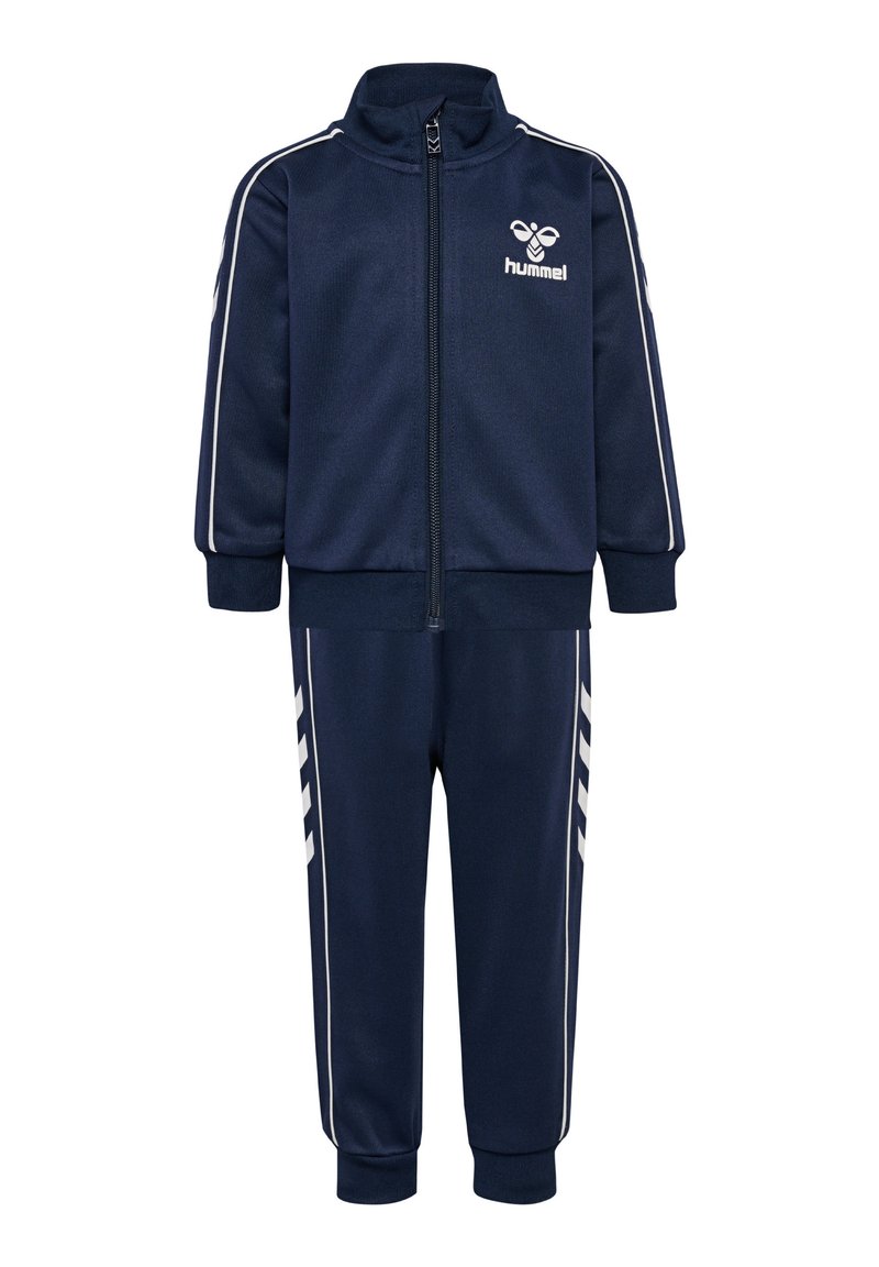 Survêtement bleu marine en tissu doux comprenant une veste zippée avec des bandes blanches et un logo, associée à un pantalon ajusté et des poignets côtelés.