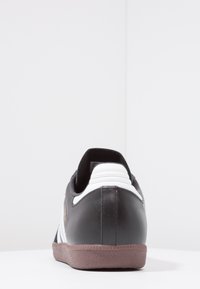 Sneaker nera con tomaia in pelle liscia, dettagli bianchi sul tallone e suola in gomma marrone testurizzata. Caratterizzato da un design a taglio basso.
