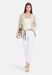 Beige Leinenblazer über einem cremefarbenen Oberteil, weißen Hosen und taupefarbene Mules. Ein gemusterter Seidenschal betont die Taille. Kleine Tasche mit Tragegurt.