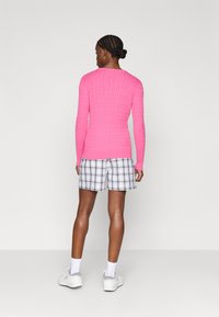 Suéter rosa ajustado com riscas e mangas longas, combinado com calções às riscas em preto e branco, acompanhado de sapatos e meias brancas.