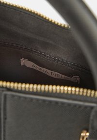 Otevřená černá kabelka s viditelným zlatým zipem a textilní štítkem uvnitř s názvem značky "ANNA FIELD".