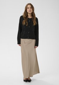 Fekete kötött kardigán foltos díszítéssel, bézs szatén maxiszoknyával és fekete hegyes orrú lapos cipővel párosítva.