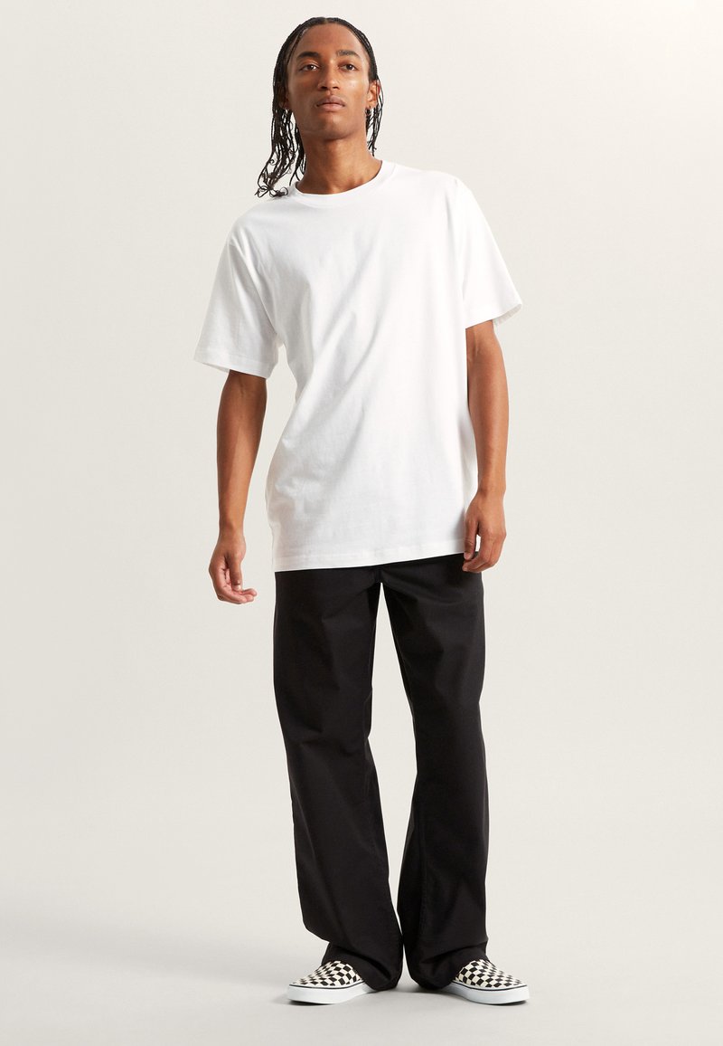 White cotton t-shirt with short sleeves, paired with black wide-leg pants and checkered slip-on shoes, on a neutral background.
