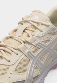 Beež ja heledarosad jooksujalatsid võrgukangaga, sünteetiliste paneelide, paelte ja kummist tallaga, millel on brändi detail keelal.