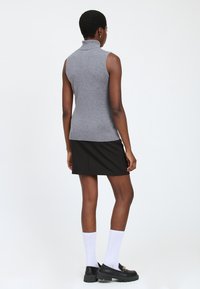 maglione grigio senza maniche a collo alto dalla vestibilità aderente, abbinato a una gonna nera. La modella indossa calze bianche a coste e scarpe nere chunky.