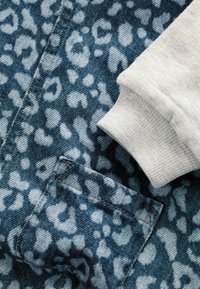 Tissu bleu avec un imprimé léopard léger et une petite poche, à côté d'un bord-côte de sweat-shirt gris clair.